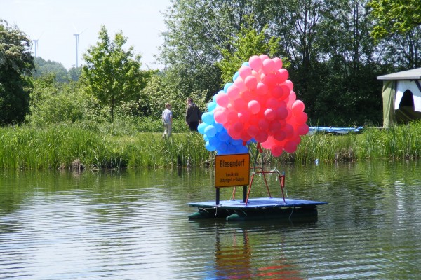 Mit Helium gefüllte Luftballons und Dorfeingangsschild auf dem Dorfteich im Pausenort Blesendorf 2010